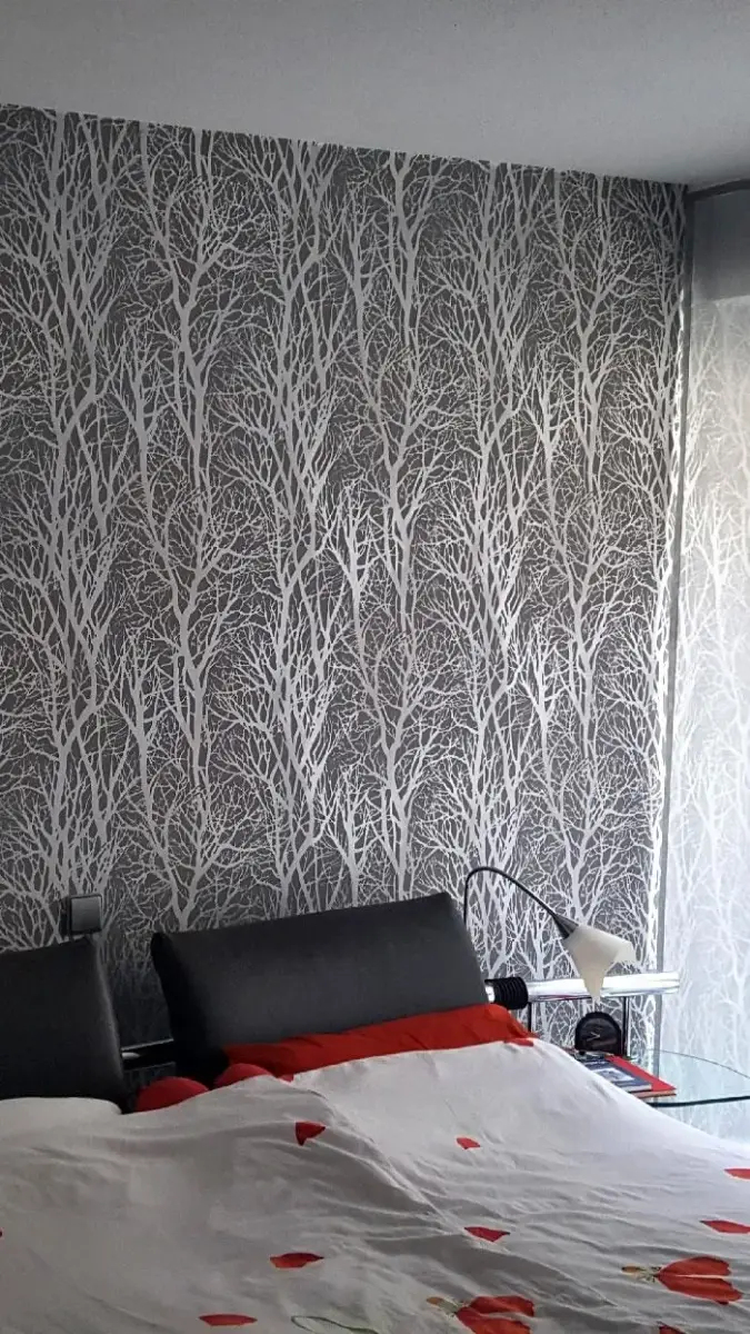 Ein Schlafzimmer mit Bett, Nachttisch, Lampe und Tapete.